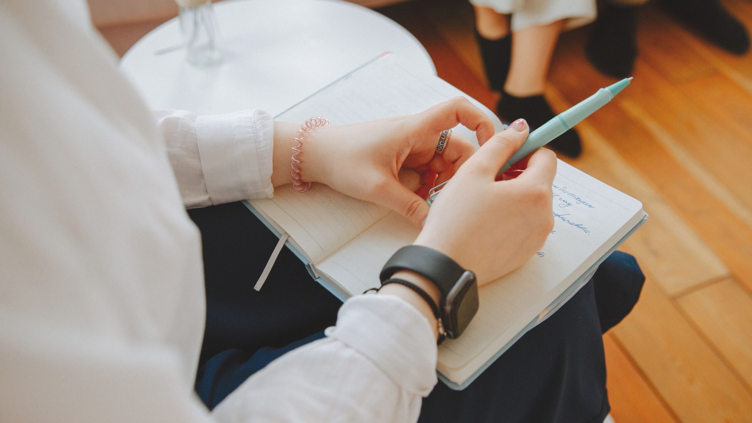 A person is sitting holding a pen and with a notebook in the lap.