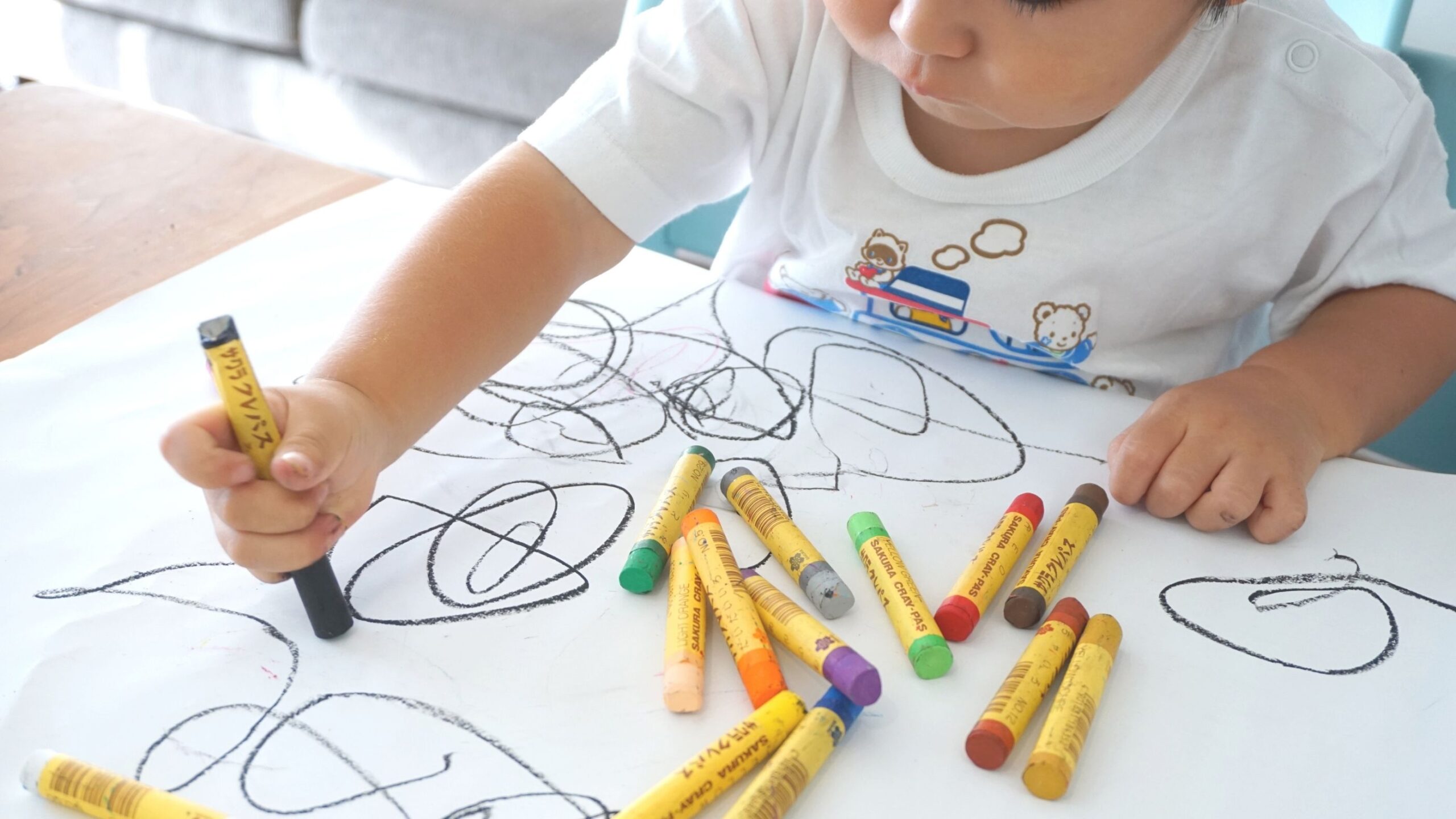 A child is drawing with crayons on a white paper.