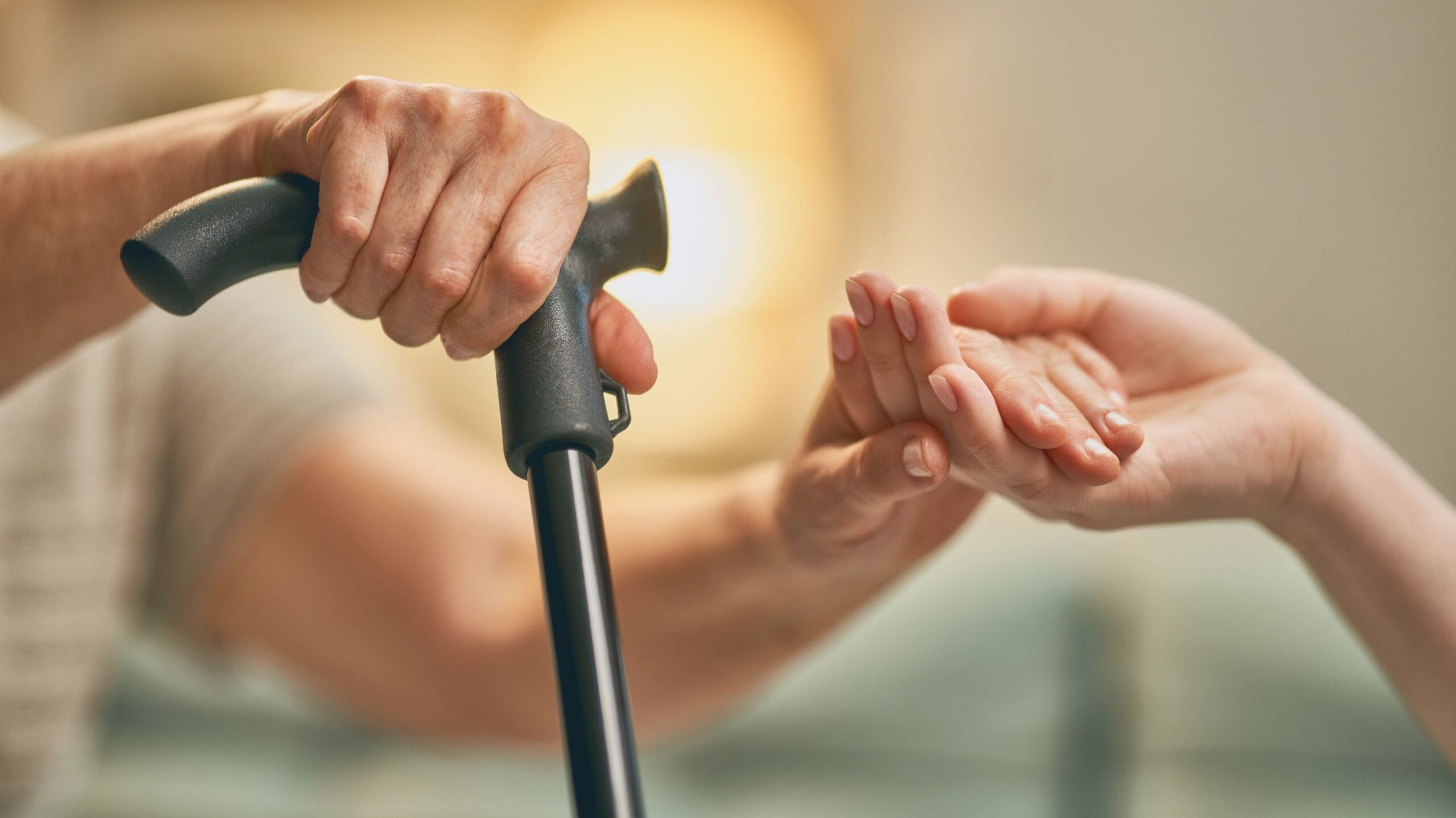 A younger hand is helping an older one with a cane.