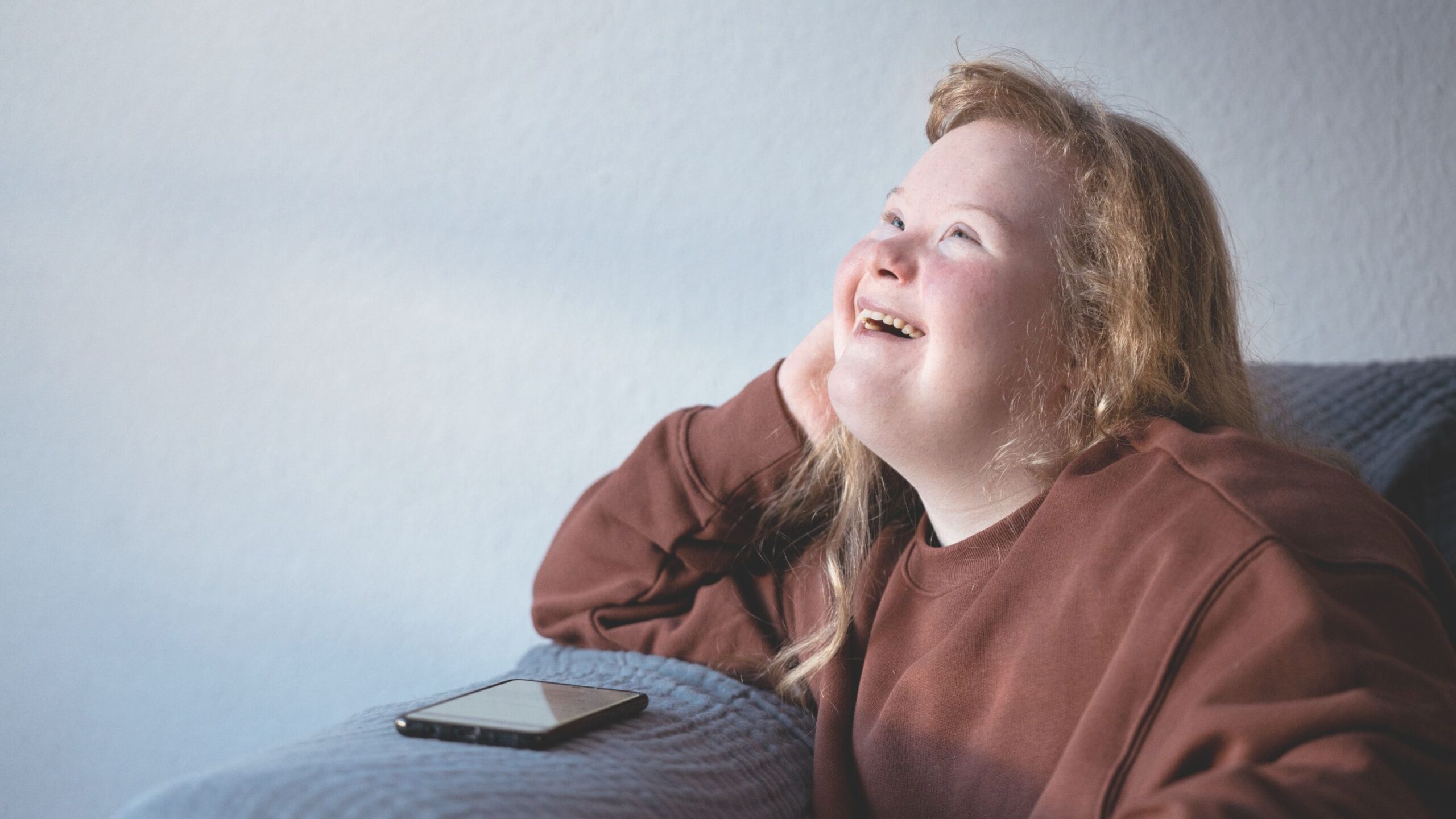 A girl is looking up and laughing with a mobile phone in front of her.