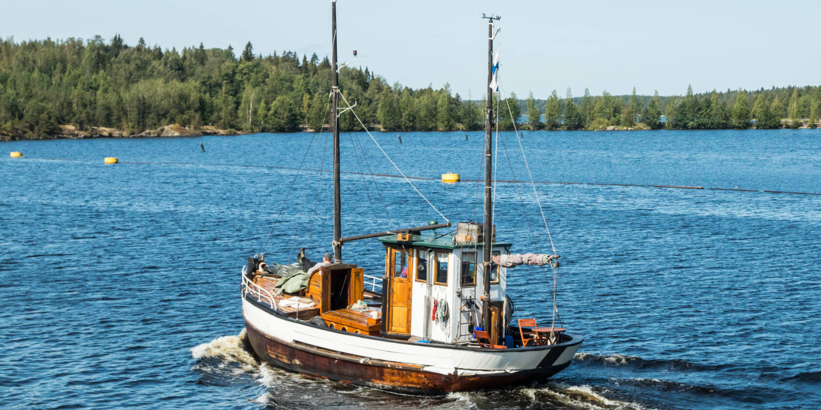 Pieni laiva kesäisellä sinisellä Saimaalla kulkee kohti saaria.
