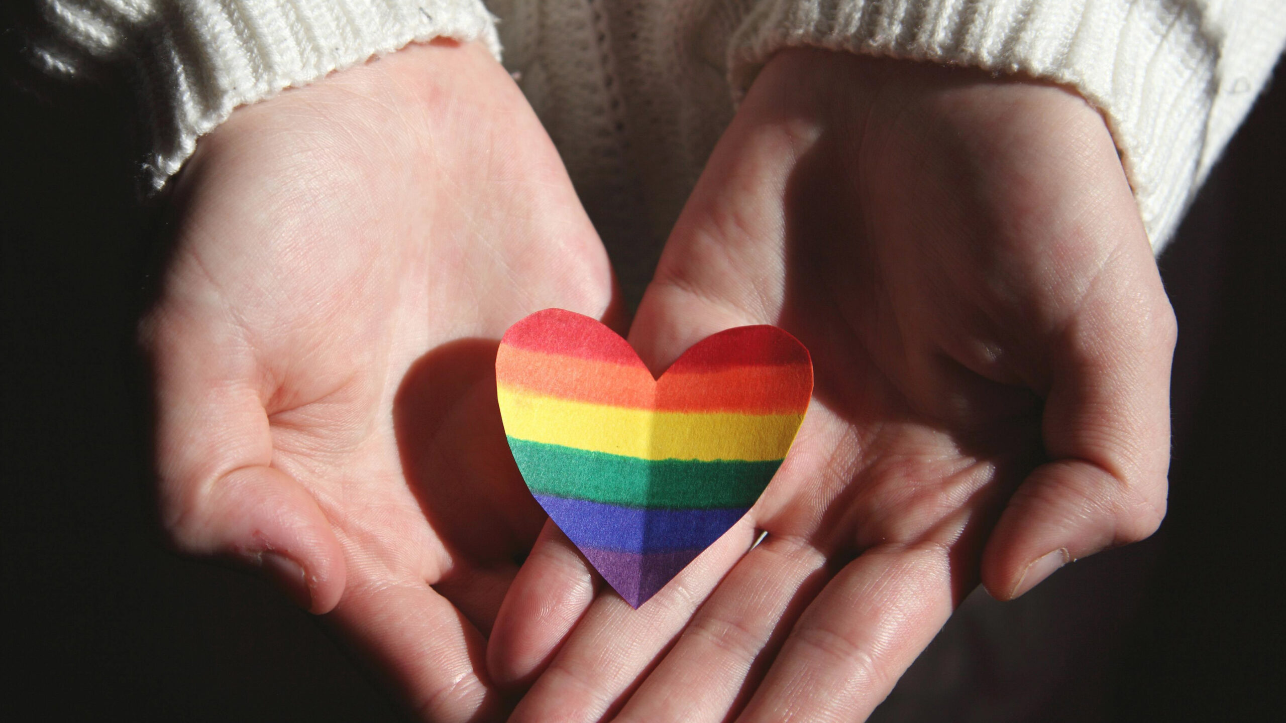 A rainbow heart in the hands of a person.