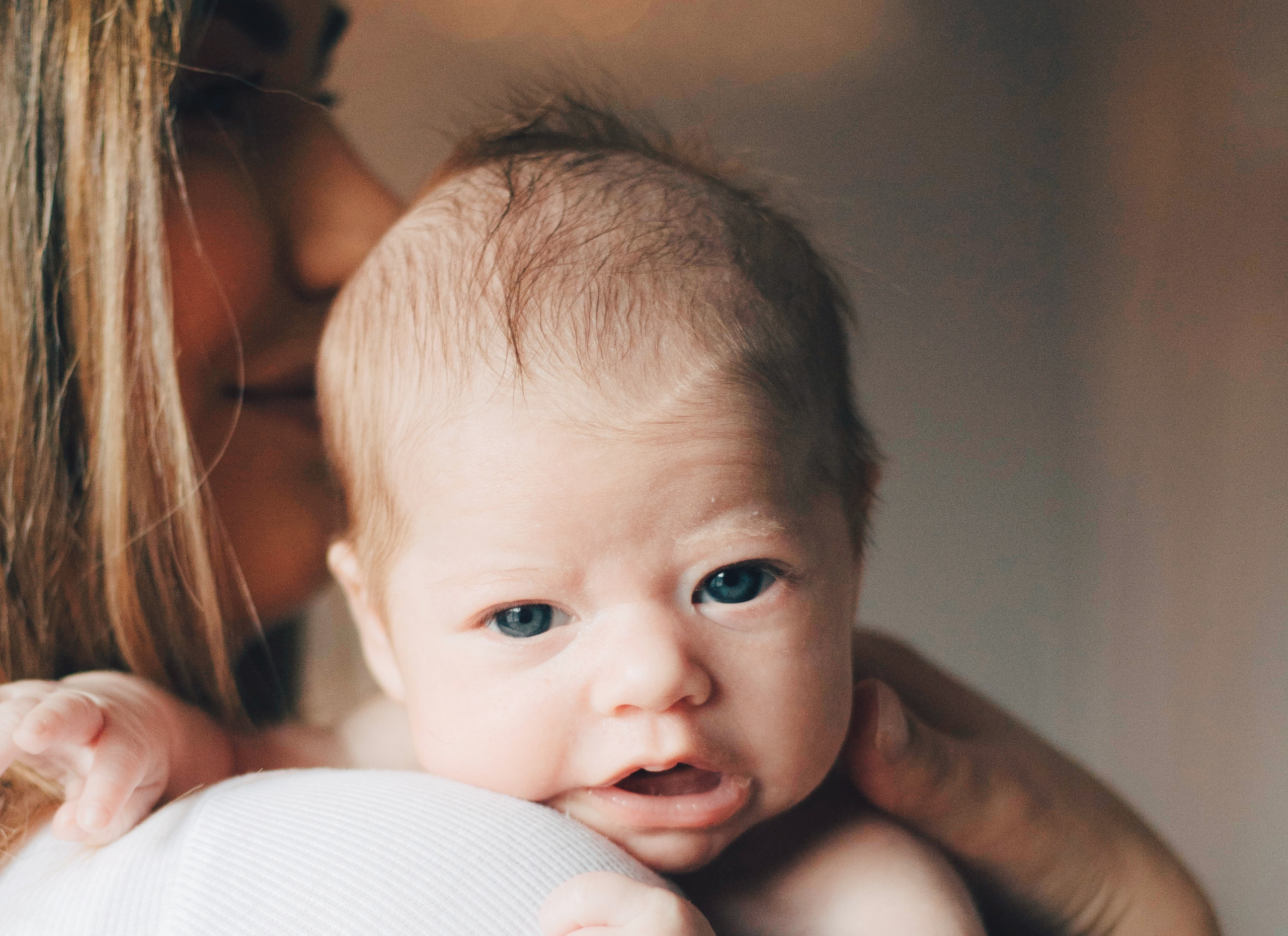 A baby on a woman's shoulder looks straight in to the camera.
