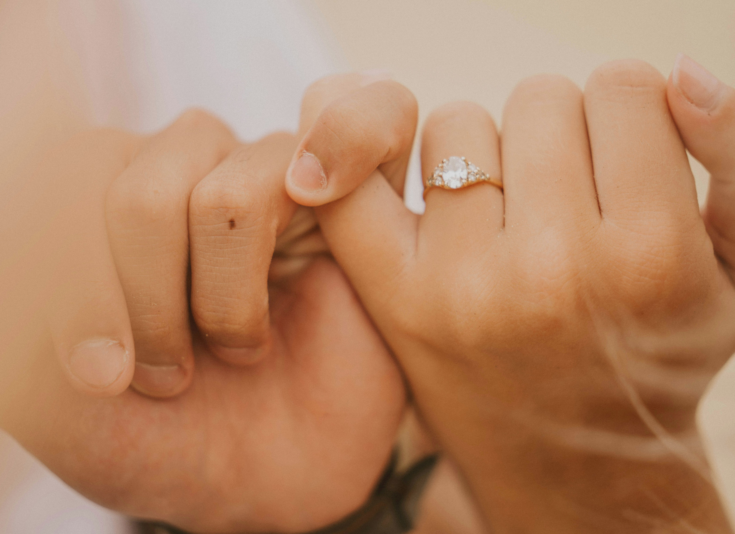 Two hands holding each other by the pinkie fingers. One hand has a diamond ring.