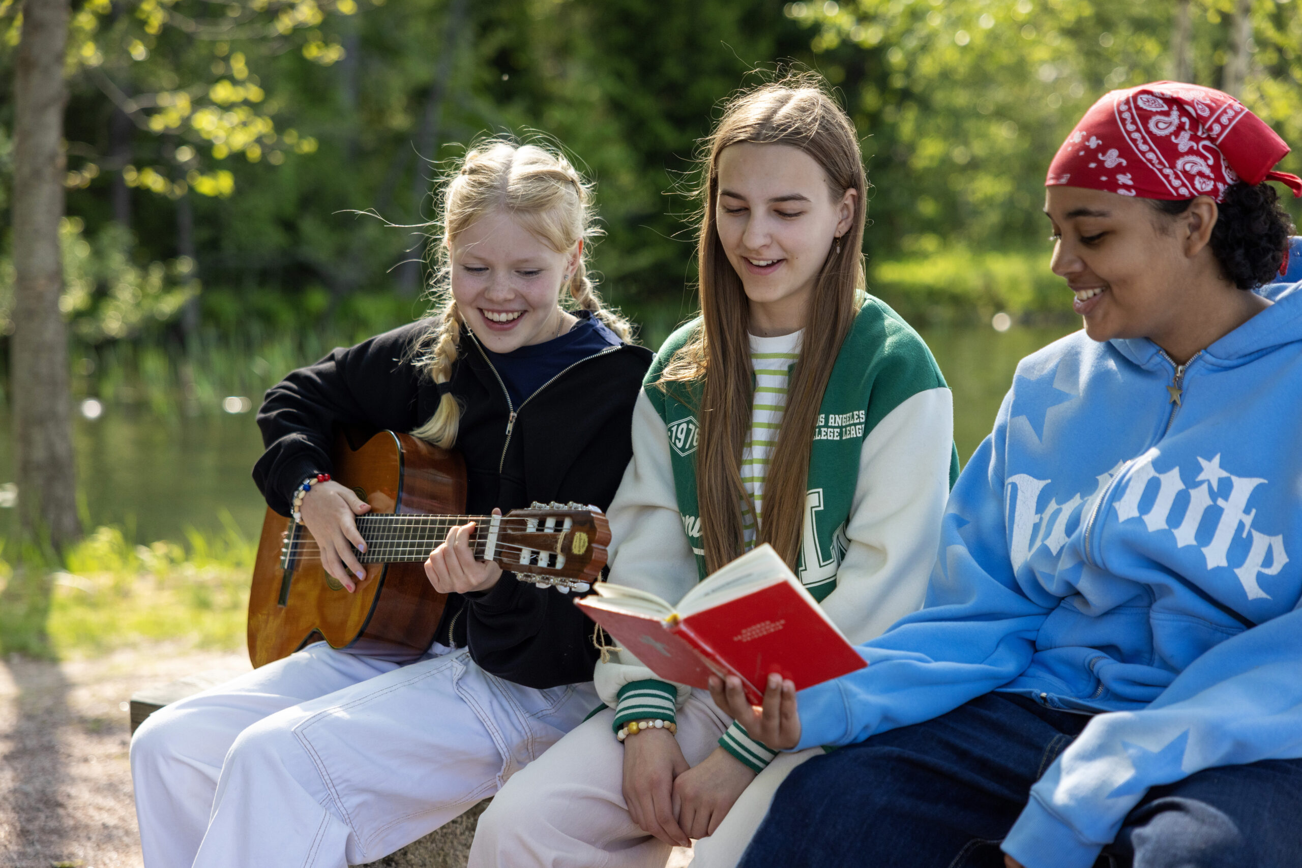 Three girls are singing. One has a guitar and another a song book.
