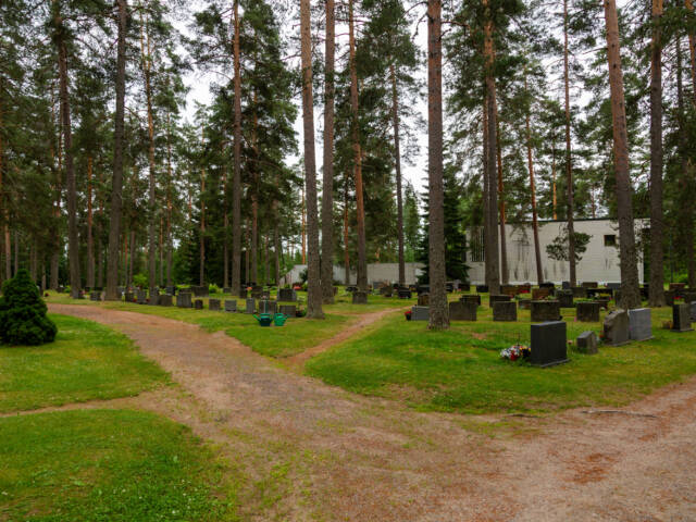 Teiden risteys edessä ja taustalla siunauskappeli puiden keskellä.