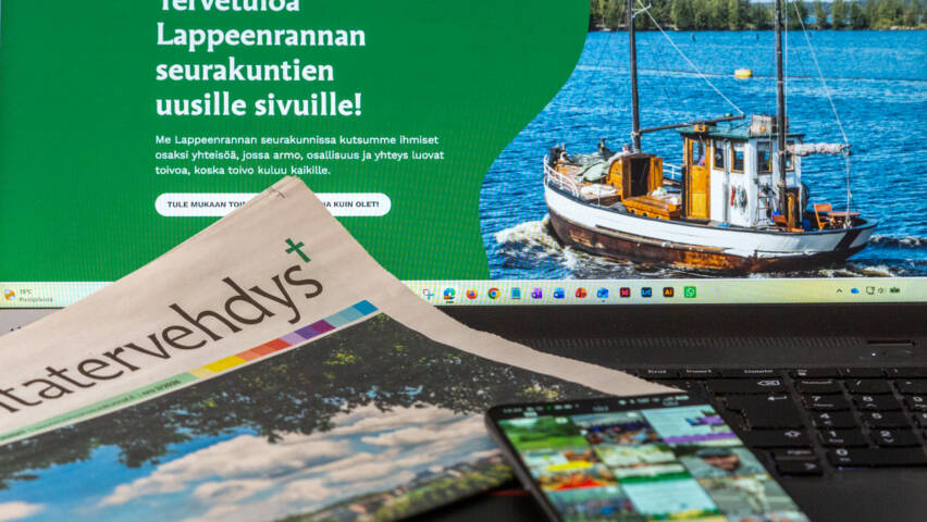 kannettavan tietokoneen näyttö, Seurakuntatervehdys-lehti ja matkapuhelin, jonka näytöllä Instagram kuvasyöte.