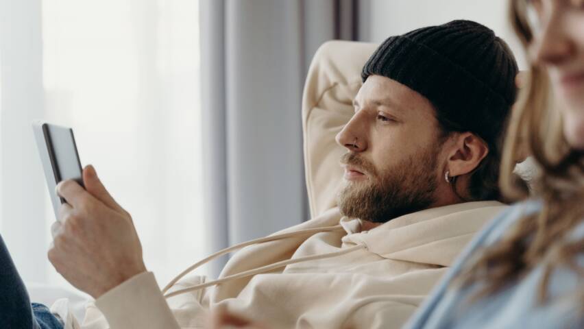 Mies istuu rennosti sohvalla ja lukee blogia tabletilta.